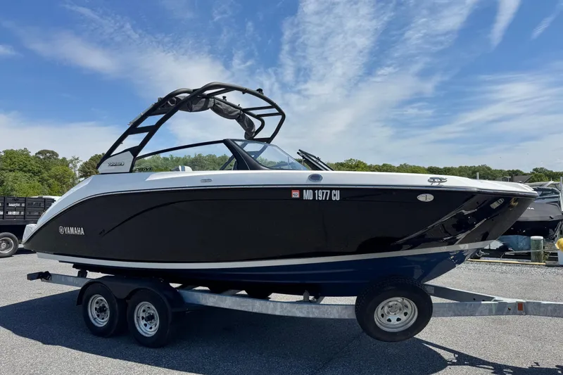 The Image of 2023 Yamaha Boats 222SD on trailer, sleek black design under clear blue sky. - 0
