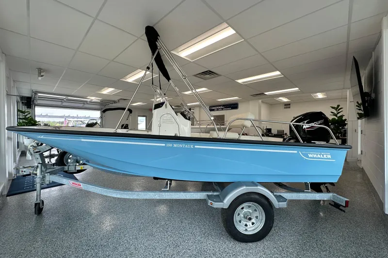 The Image of 2026 Boston Whaler 150 Montauk boat in showroom, blue hull on trailer. - 16
