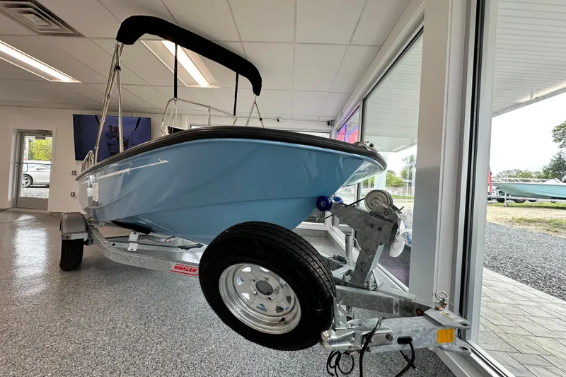 Slide: The Image of 2026 Boston Whaler 150 Montauk boat displayed indoors on a trailer. - 18