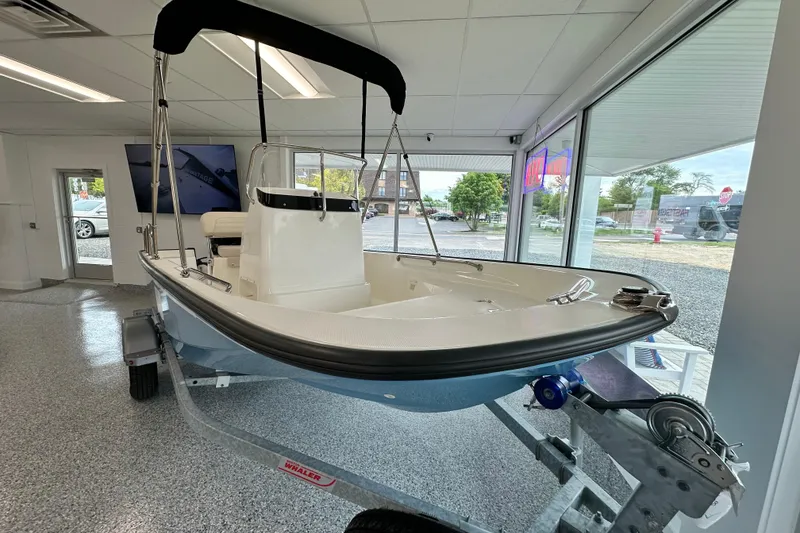 Slide: The Image of 2026 Boston Whaler 150 Montauk boat displayed indoors on a trailer. - 19