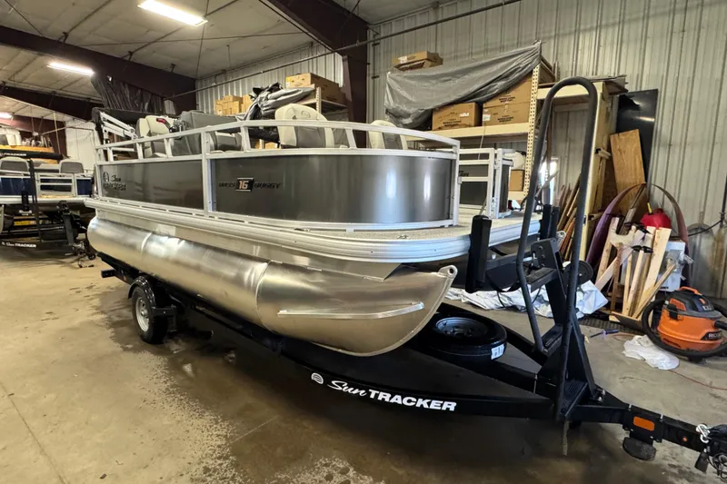 Slide: The Image of 2026 Sun Tracker Bass Buggy 16 XL Select pontoon boat in a storage facility. - 2