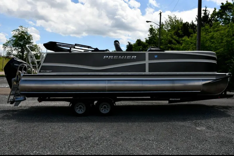 Slide: The Image of 2024 Premier 250 RL PTX pontoon boat on trailer, parked outdoors under cloudy sky. - 2
