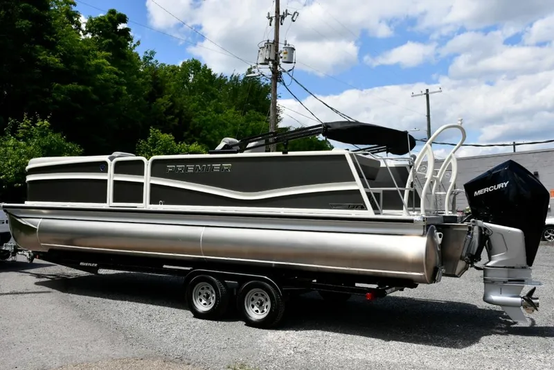 Slide: The Image of 2024 Premier 250 RL PTX pontoon boat with Mercury engine, parked outdoors. - 3