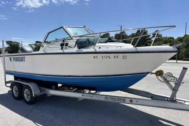 Slide: The Image of 1989 Pursuit 2260 Denali boat on trailer, parked outdoors under clear sky. - 18