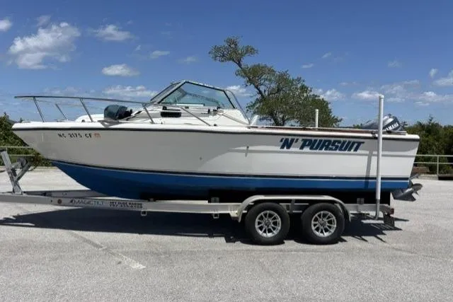 Slide: The Image of 1989 Pursuit 2260 Denali boat on trailer, parked outdoors under a clear blue sky. - 25