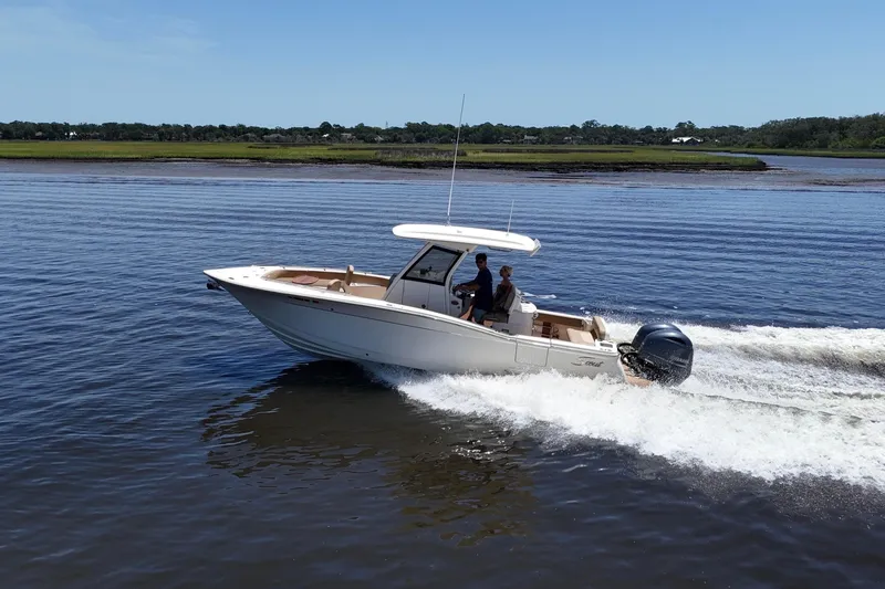 Slide: The Image of 2021 Scout 277 LXF boat cruising on a calm river under clear blue skies. - 0