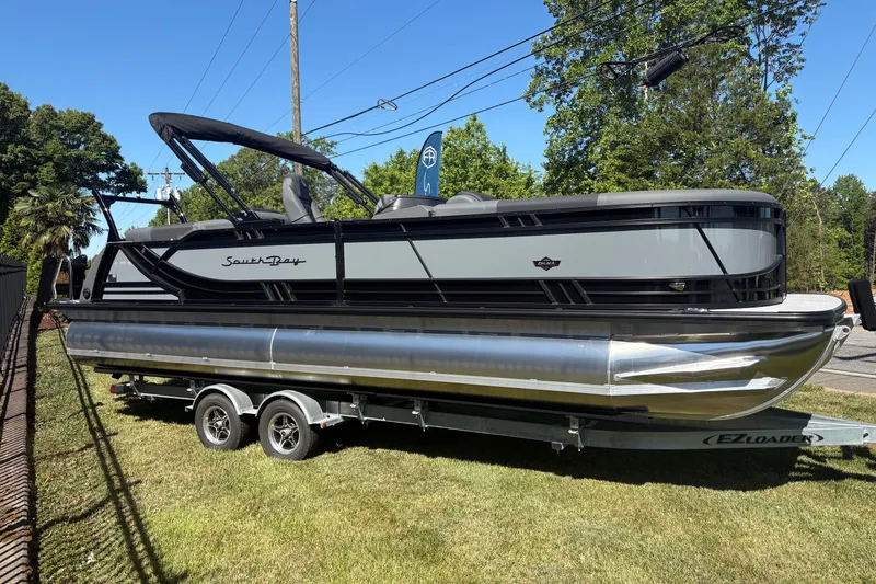 The Image of 2026 South Bay 525RS pontoon boat on trailer, parked on grass, under clear blue sky. - 0