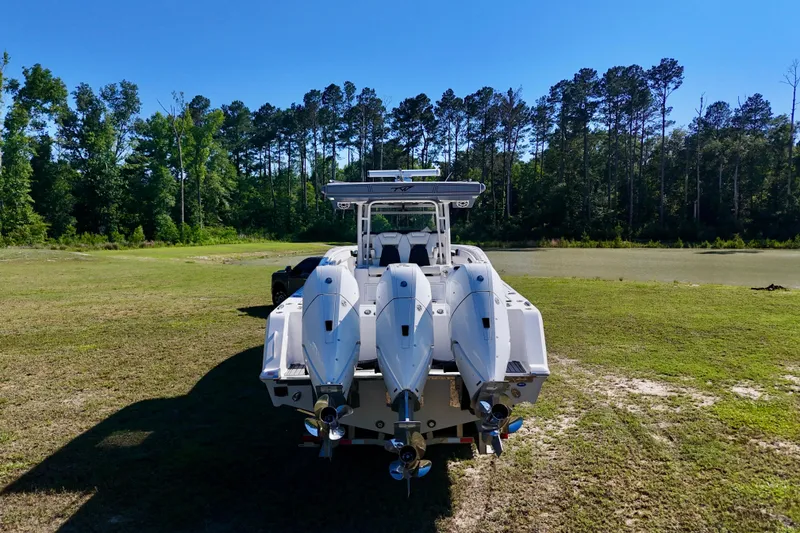 Slide: The Image of 2024 Tidewater 380 CC Adventure boat with triple engines, parked on grassy terrain near a forest. - 12