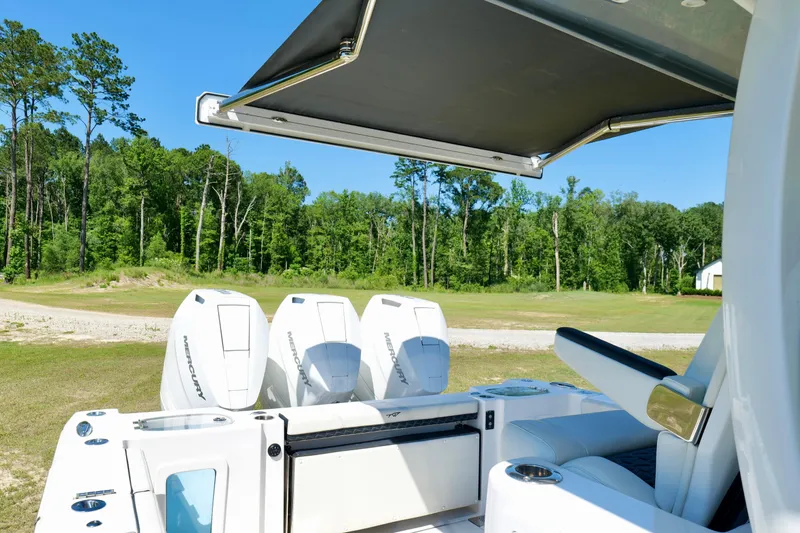 Slide: The Image of 2024 Tidewater 380 CC Adventure boat with triple Mercury engines, shaded seating, and lush green backdrop. - 28