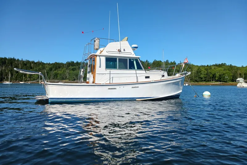 Slide: The Image of 1989 Cape Dory Flybridge Cruiser on calm water, surrounded by lush greenery. - 21