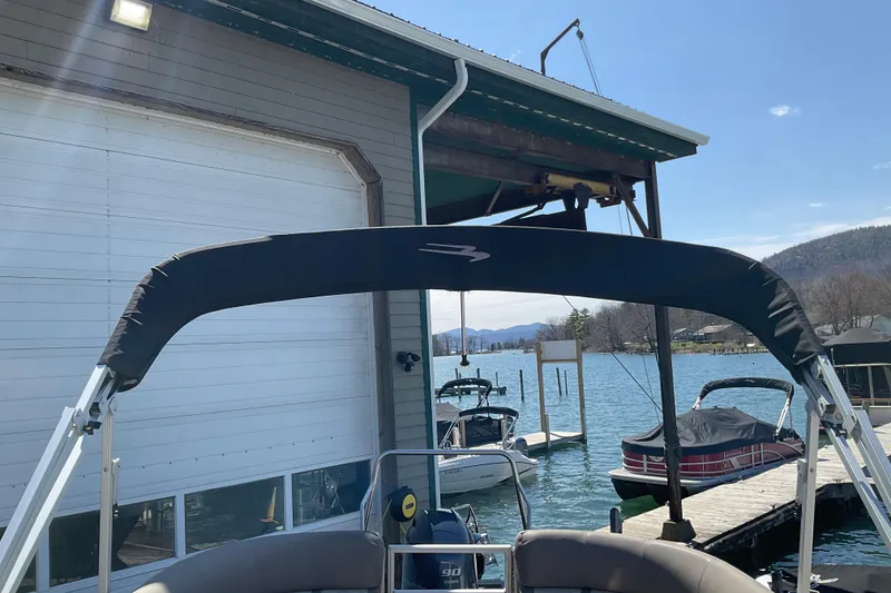 Slide: The Image of 2019 Bennington SX 20 SSRX pontoon boat docked by a lakeside boathouse. - 24