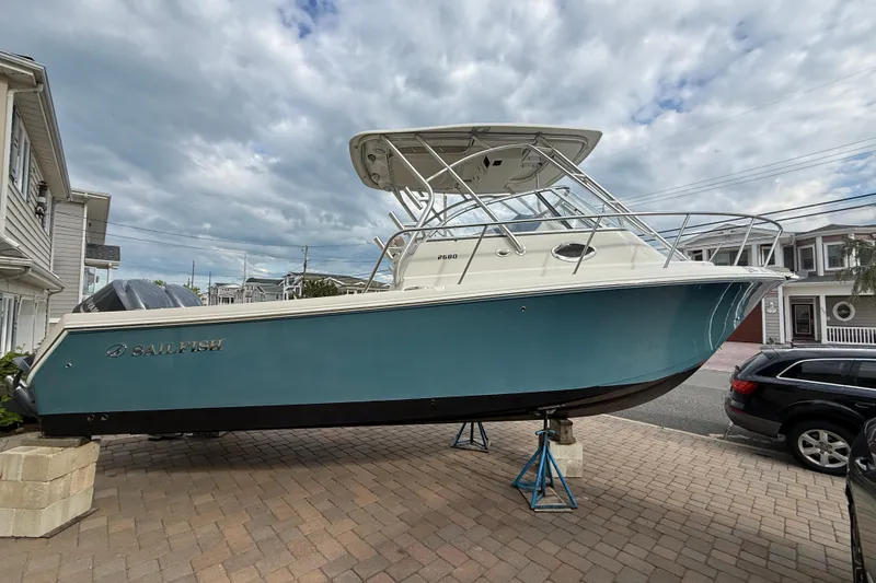 The Image of 2012 Sailfish 2680 WAC boat on stands, parked in a residential driveway under cloudy skies. - 0