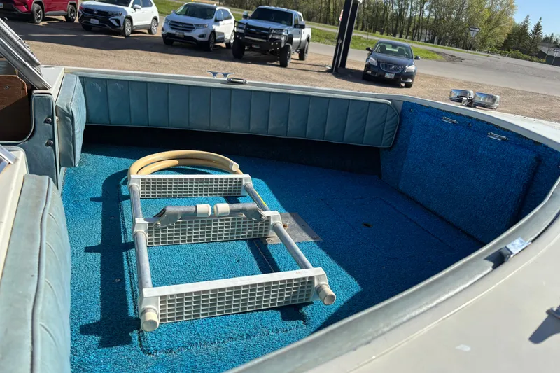 Slide: The Image of 1983 Crestliner 16 boat interior with blue carpet and ladder, parked near vehicles. - 10