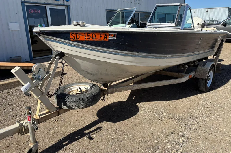 Slide: The Image of 1983 Crestliner 16 boat on trailer, parked outside a building with an "Open" sign. - 2