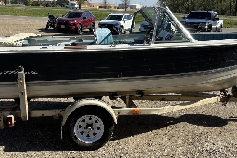 Slide: The Image of 1983 Crestliner 16 boat on trailer, parked in a lot with cars and motorcycle nearby. - 6