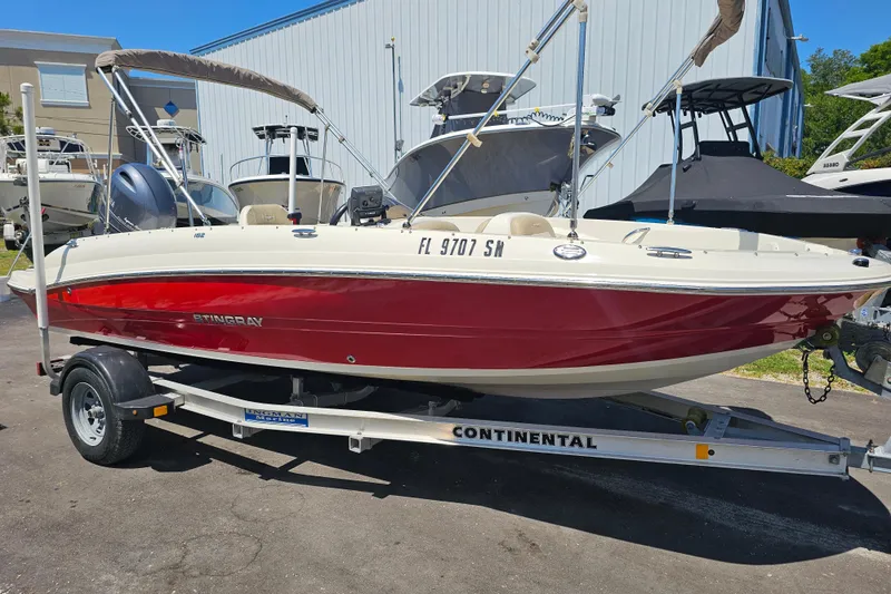Slide: The Image of 2019 Stingray 182 SC boat on trailer, red and white exterior, parked outdoors. - 2