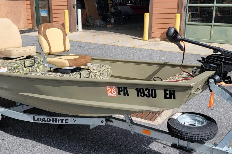 The Image of 2025 Tracker Grizzly 12 Jon boat on trailer, featuring camouflage seats and electric motor. - 1
