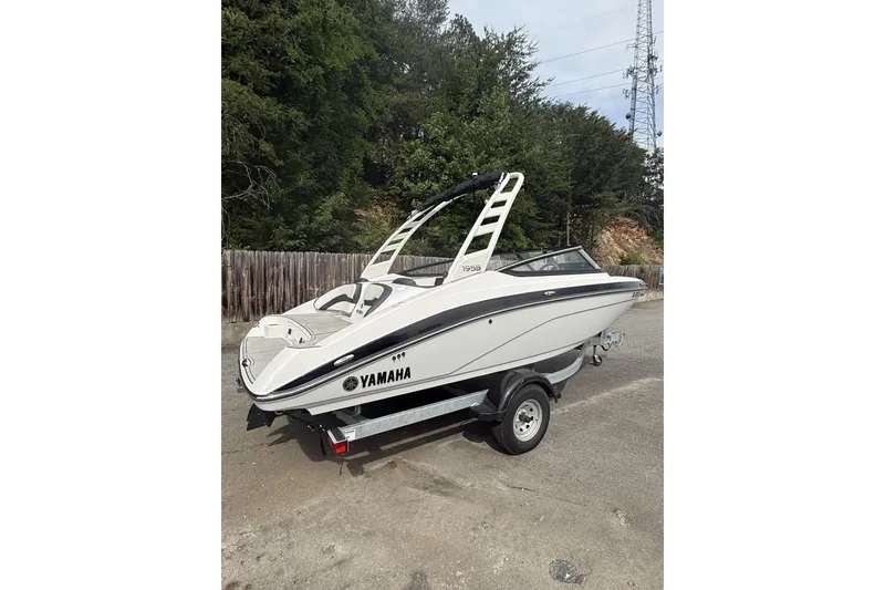 The Image of 2025 Yamaha Boats 195S on trailer, parked outdoors with trees in background. - 0