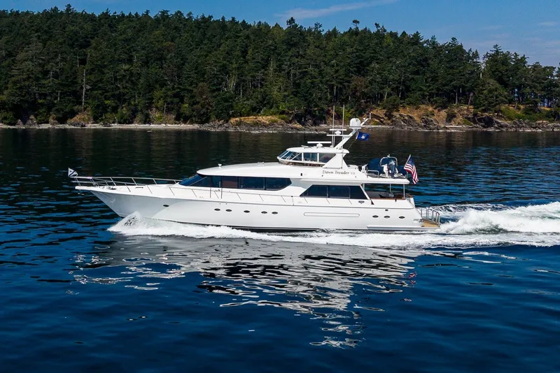 The Image of 2005 West Bay 86 Raised Pilothouse Motor Yacht cruising on calm waters near a forested shoreline. - 0