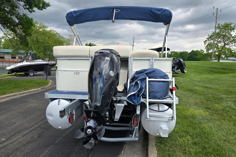 Slide: The Image of 2004 Odyssey Pontoons 2302 Millennium boat with outboard motor, parked on a paved area. - 2