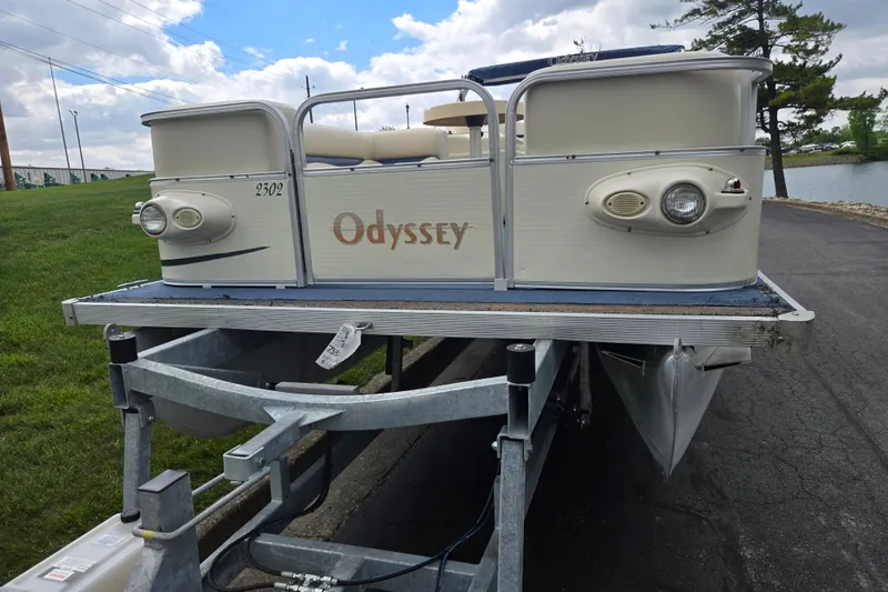 Slide: The Image of 2004 Odyssey Pontoons 2302 Millennium on trailer, parked near a lake under a cloudy sky. - 6