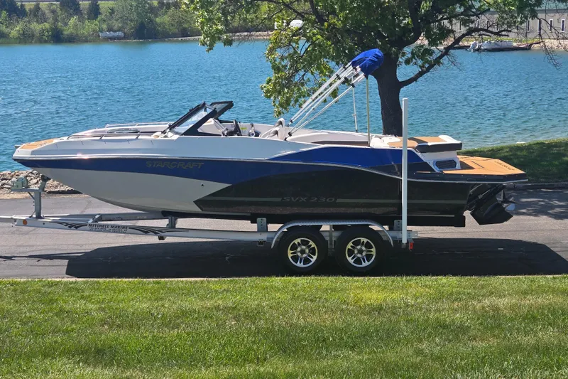 The Image of 2023 Starcraft SVX 230 IO boat on trailer by a scenic lake. - 0