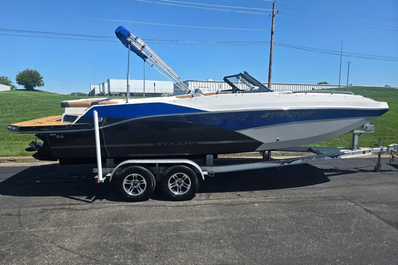 Slide: The Image of 2023 Starcraft SVX 230 IO boat on trailer, parked outdoors under clear blue sky. - 4