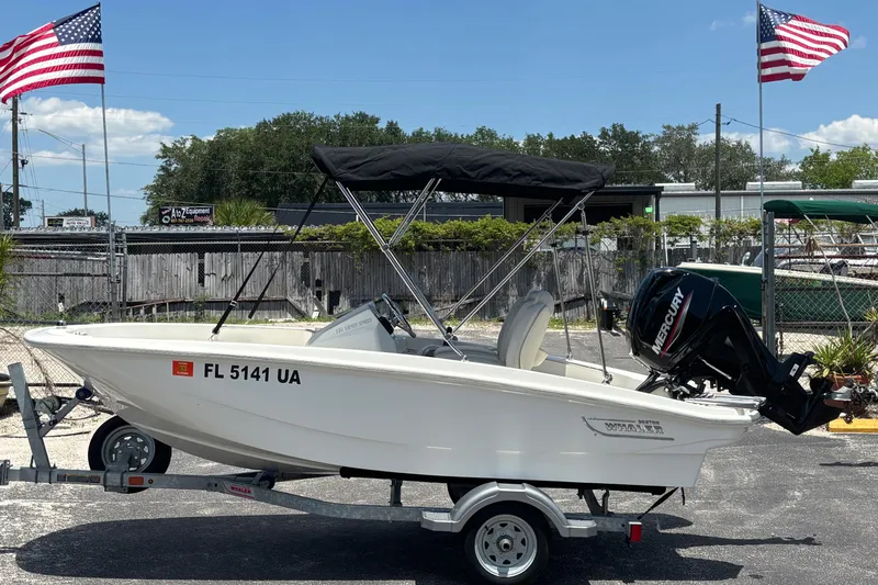 Slide: The Image of 2025 Boston Whaler 130 Super Sport boat on trailer, with American flags in the background. - 1