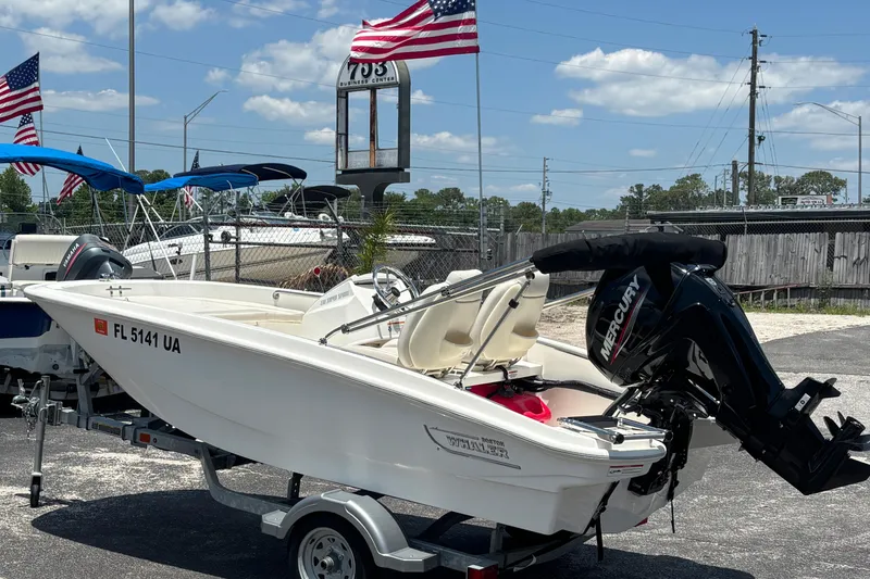 Slide: The Image of 2025 Boston Whaler 130 Super Sport boat on trailer, with Mercury engine, American flags in background. - 3