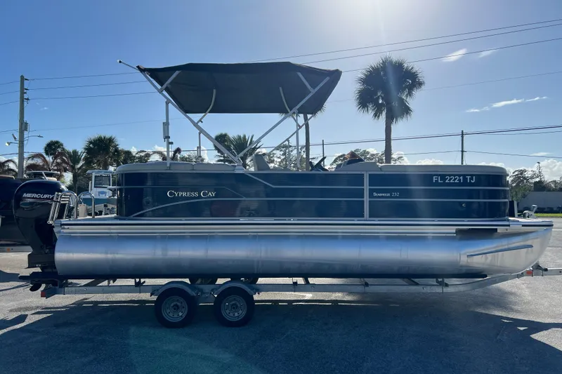 The Image of 2023 Cypress Cay Seabreeze 232 pontoon boat on trailer, sunny day, palm trees in background. - 1