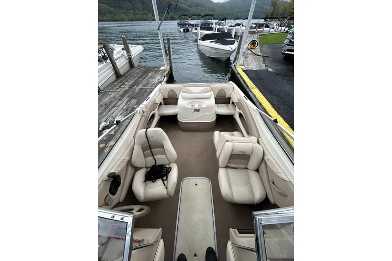 Slide: The Image of 2001 Stingray 200 LS/LX boat interior with beige seating, docked by a scenic lake. - 13