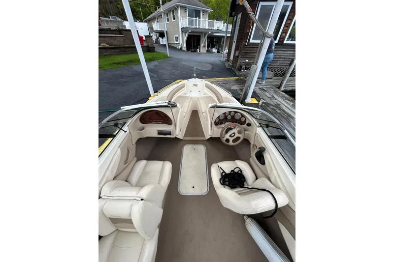 Slide: The Image of 2001 Stingray 200 LS/LX boat interior with beige seating and dashboard, docked near a house. - 14