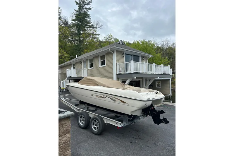 Slide: The Image of 2001 Stingray 200 LS/LX boat on trailer, parked near a house with greenery. - 5