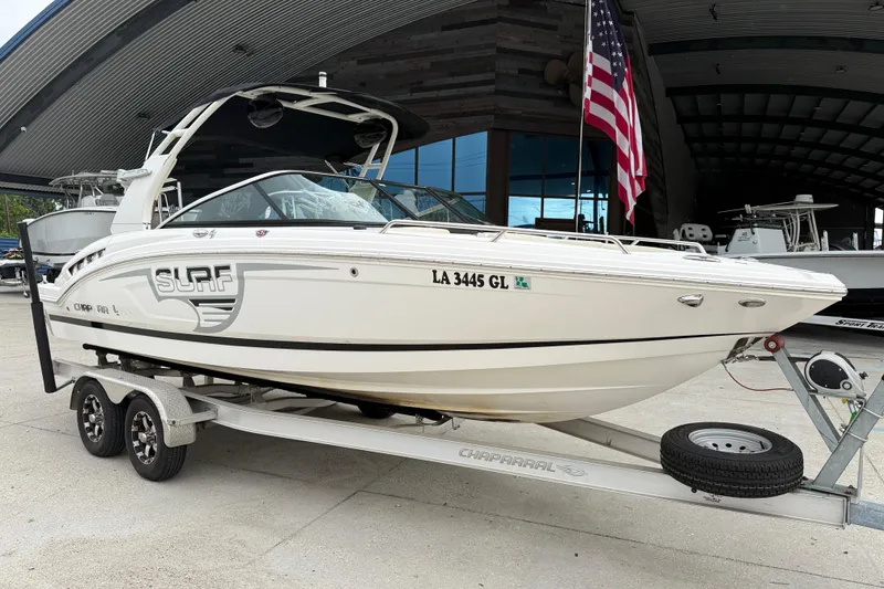 Slide: The Image of 2018 Chaparral 227 SSX Surf boat on trailer, parked near a building with an American flag. - 2