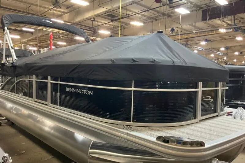 Slide: The Image of 2026 Bennington 23 SX L-Bench pontoon boat with cover in a showroom setting. - 1