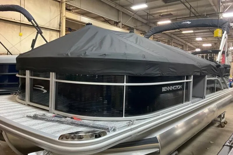Slide: The Image of 2026 Bennington 23 SX L-Bench pontoon boat with cover in a warehouse setting. - 2