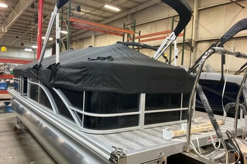Slide: The Image of 2026 Bennington 23 SX L-Bench pontoon boat with black cover in a warehouse setting. - 3