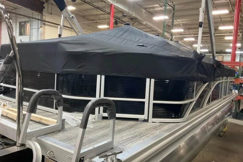 Slide: The Image of 2026 Bennington 23 SX L-Bench pontoon boat with black cover in a warehouse setting. - 4
