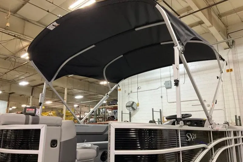 Slide: The Image of 2026 Bennington 23 SX L-Bench pontoon boat with black canopy in warehouse setting. - 6