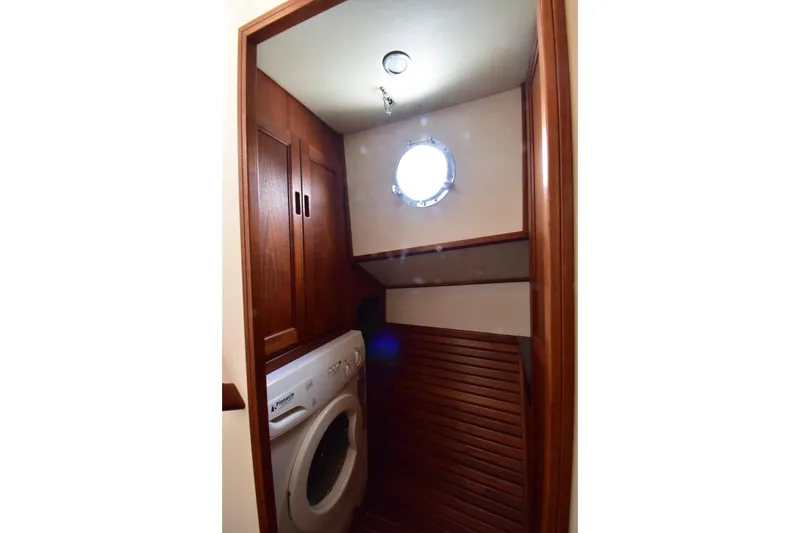 Slide: The Image of Laundry area with washer in 2007 Nordic Tug 37 boat, featuring wooden cabinetry and porthole window. - 22