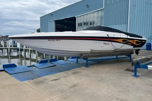 Slide: The Image of 2000 Donzi 33 ZX speedboat with flame decals, docked near a blue warehouse. - 2
