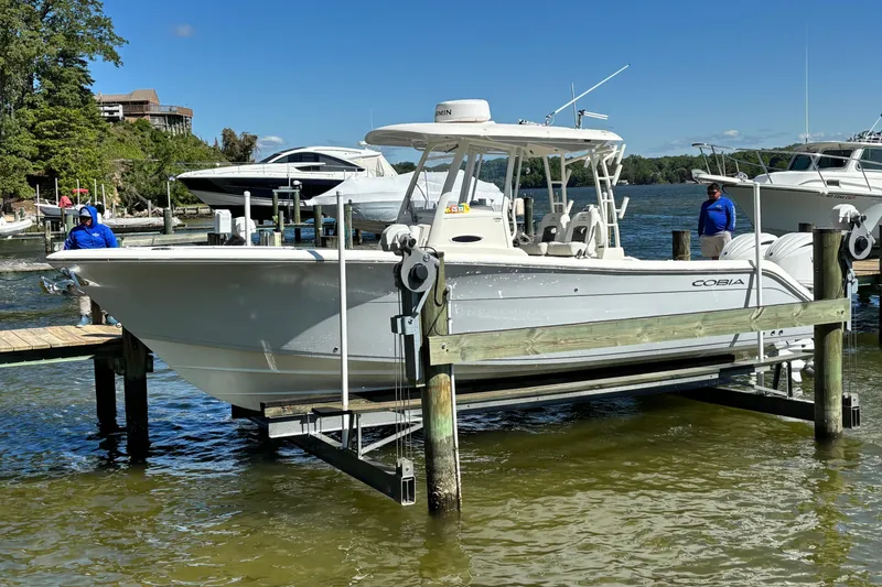 The Image of 2023 Cobia 301 Center Console boat on lift at marina, clear sky background. - 0