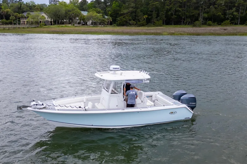 Slide: The Image of 2014 Sea Hunt Gamefish 27 boat on calm water near a wooded shoreline. - 16