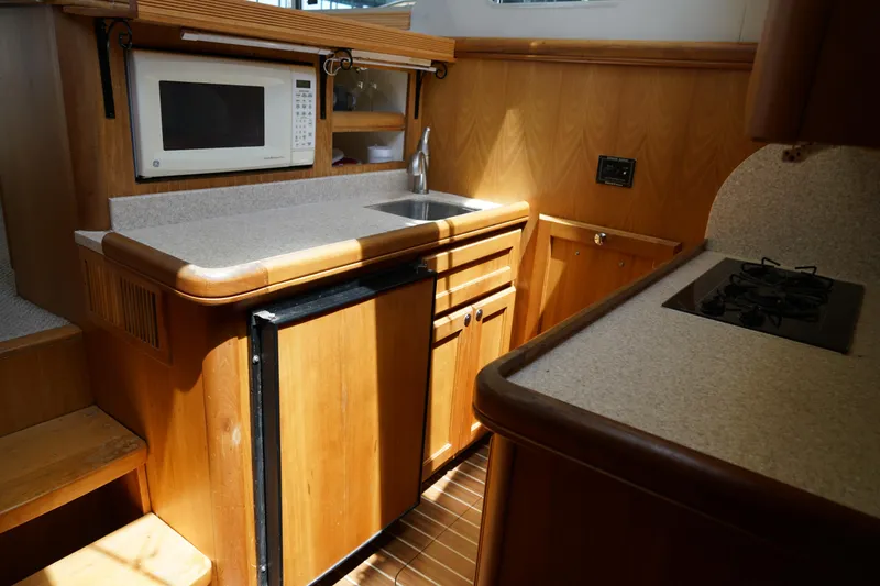 Slide: The Image of Compact Mainship boat kitchen with microwave, sink, fridge, and stove, featuring wooden cabinetry. - 18