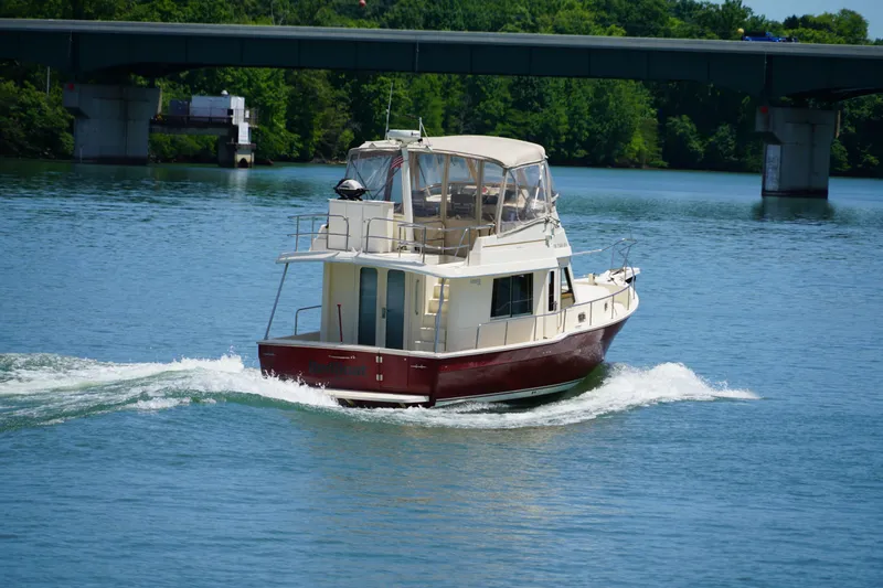 Slide: The Image of Mainship boat cruising on a river with a bridge and lush greenery in the background. - 6