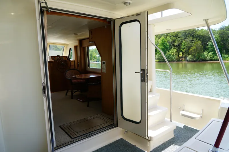 Slide: The Image of Mainship boat interior with open door, showing helm and seating area by a serene lake. - 8