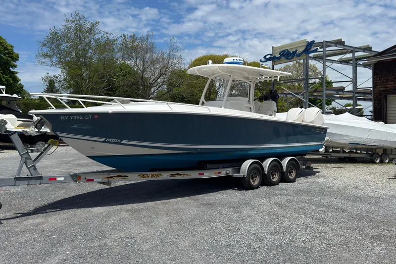 Slide: The Image of 2013 Jupiter 32 Cuddy boat on trailer, parked outdoors under a partly cloudy sky. - 2