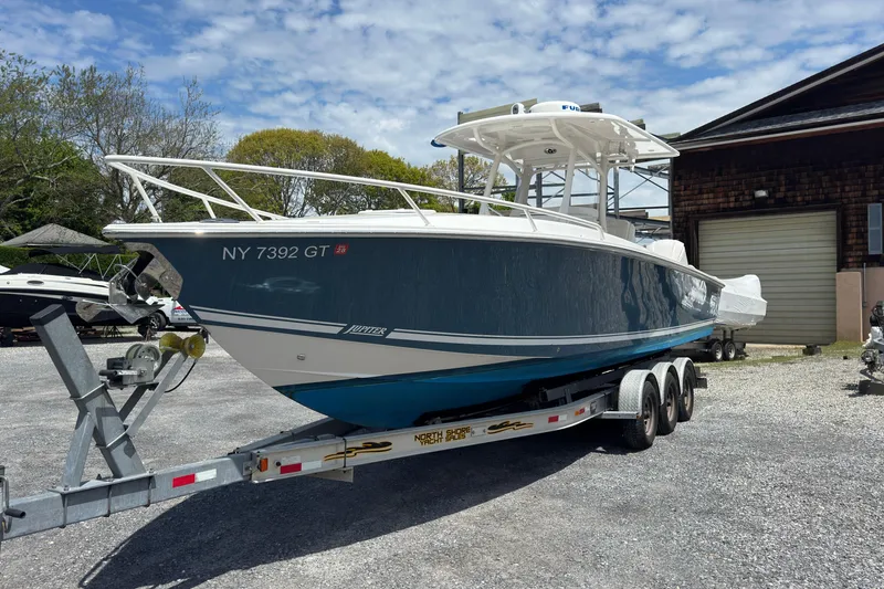 Slide: The Image of 2013 Jupiter 32 Cuddy boat on trailer, parked outdoors under a partly cloudy sky. - 3