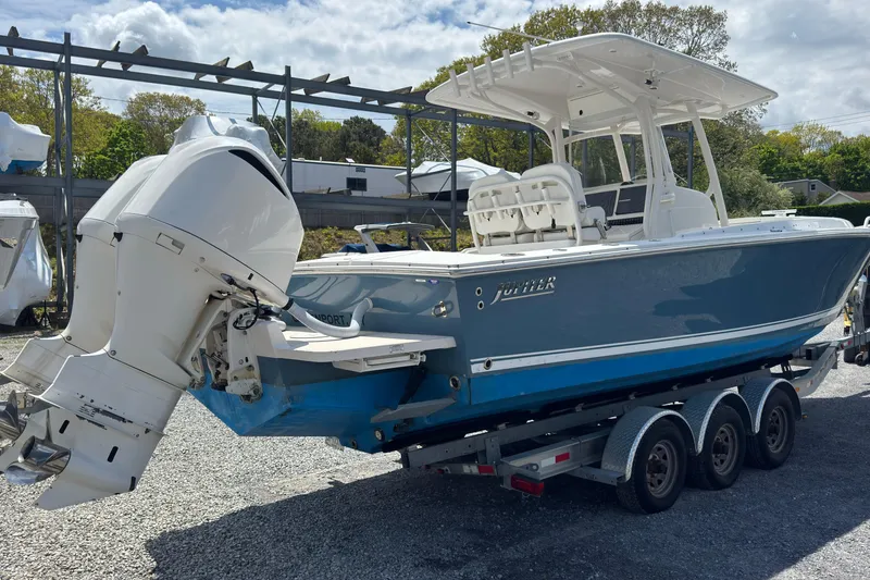 Slide: The Image of 2013 Jupiter 32 Cuddy boat on trailer, featuring dual outboard engines, parked outdoors. - 6