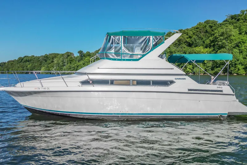 Slide: The Image of 1994 Carver 380 Santego yacht on a serene lake with lush green backdrop. - 2